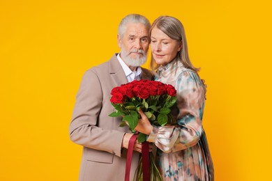 Photo of Happy couple with bouquet of red roses on yellow background