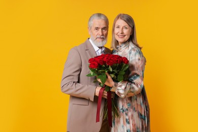 Photo of Happy couple with bouquet of red roses on yellow background