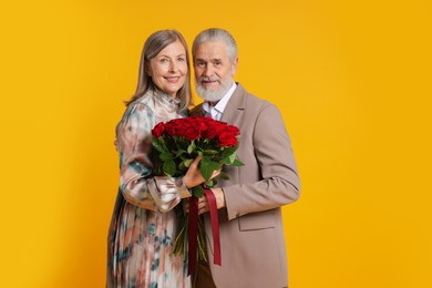 Photo of Happy couple with bouquet of red roses on yellow background