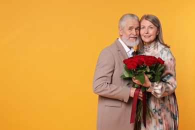 Photo of Happy couple with bouquet of red roses on yellow background. Space for text