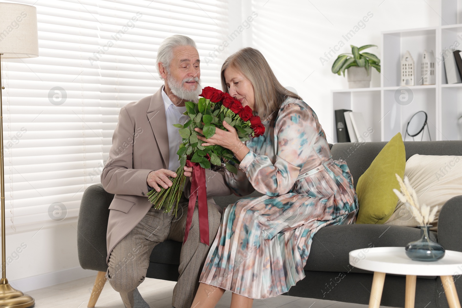 Photo of Man presenting bouquet of roses to his wife on sofa at home