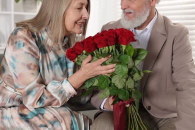 Photo of Happy couple with bouquet of red roses at home, closeup