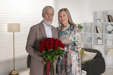 Photo of Happy couple with bouquet of red roses at home