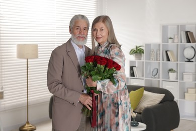 Photo of Happy couple with bouquet of red roses at home