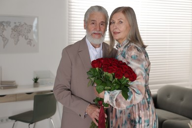 Photo of Cute couple with bouquet of red roses at home