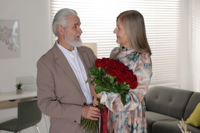 Photo of Cute couple with bouquet of red roses at home