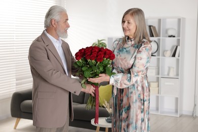 Photo of Happy couple with bouquet of red roses at home