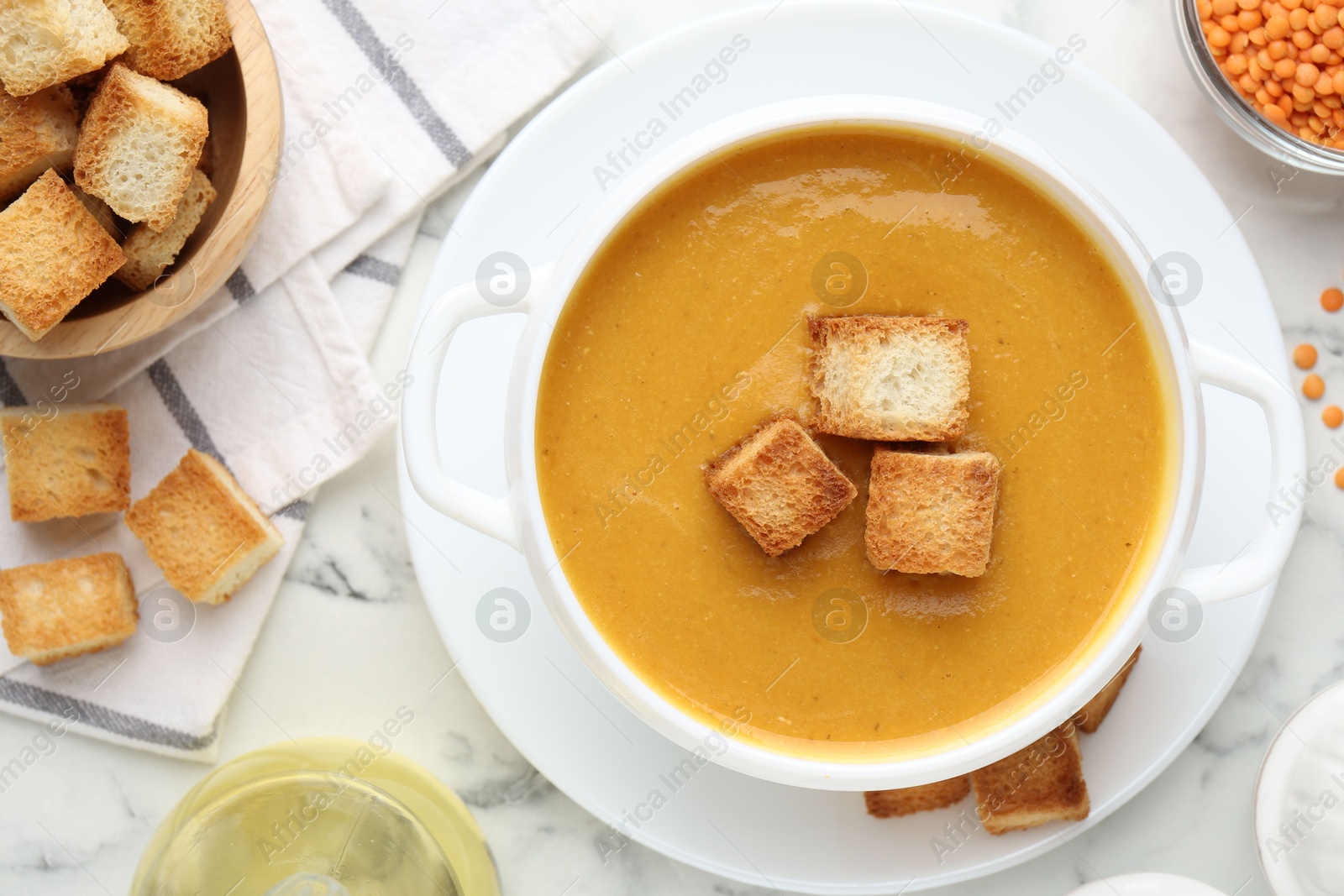 Photo of Delicious lentil cream soup served with croutons on white marble table, flat lay