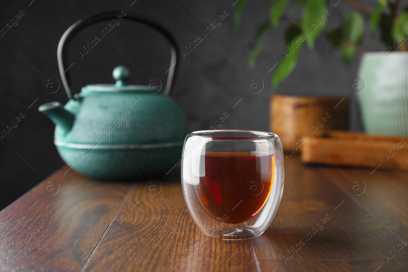 Freshly brewed tea in glass cup and teapot on wooden table Photo of Freshly brewed tea in glass cup and teapot on wooden table
