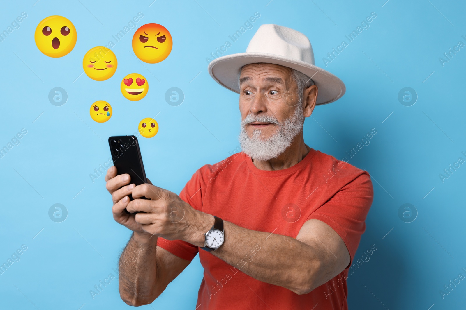 Image of Social media. Surprised senior man using mobile phone on light blue background. Different emojis near gadget