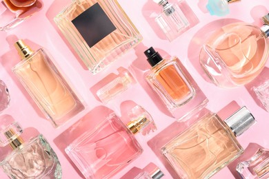 Photo of Bottles of various perfumes on pink background, flat lay