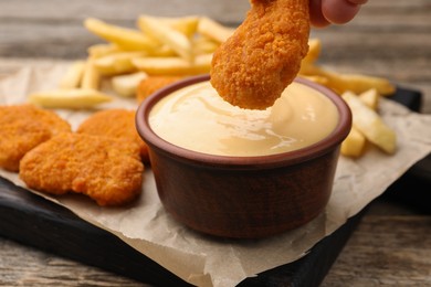 Photo of Woman dipping chicken nugget into cheese sauce at wooden table, closeup