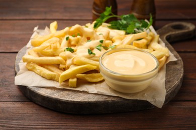 Photo of Delicious cheese sauce in bowl, French fries and parsley on wooden table, closeup