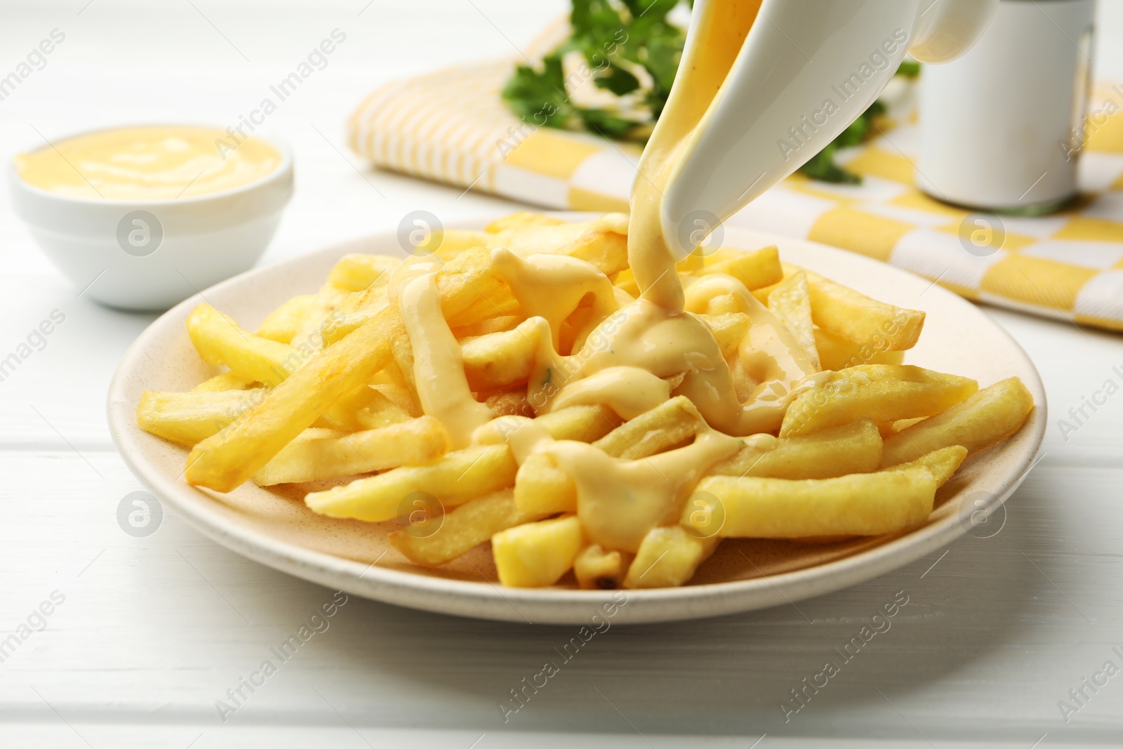Photo of Pouring delicious cheese sauce onto French fries at wooden table, closeup