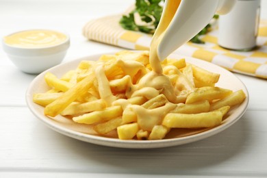 Photo of Pouring delicious cheese sauce onto French fries at wooden table, closeup