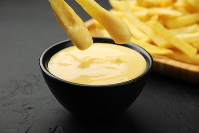 Photo of Dipping French fries into cheese sauce at black table, closeup