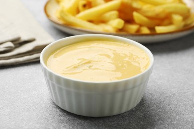 Photo of Tasty cheese sauce in bowl and French fries on grey table, closeup