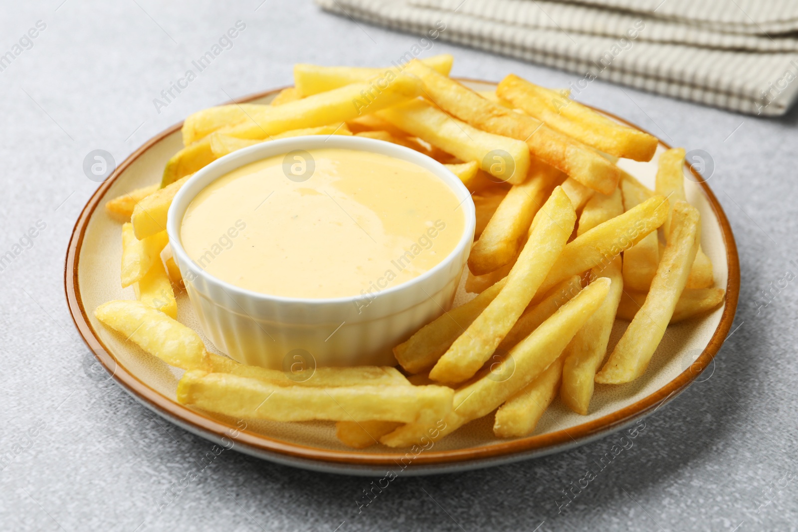Tasty cheese sauce in bowl and French fries on grey table, closeup Photo of Tasty cheese sauce in bowl and French fries on grey table, closeup
