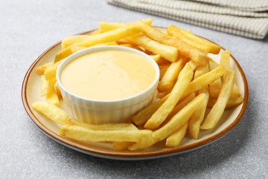 Photo of Tasty cheese sauce in bowl and French fries on grey table, closeup