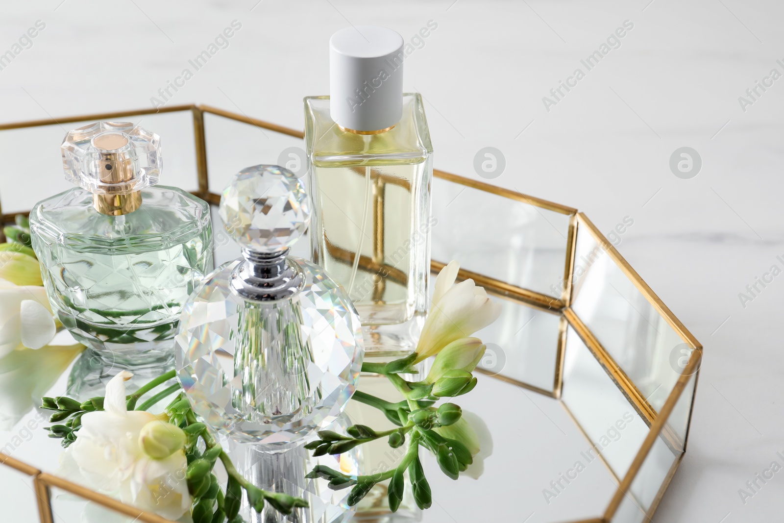 Tray with perfumes and beautiful flowers on white table, closeup Photo of Tray with perfumes and beautiful flowers on white table, closeup