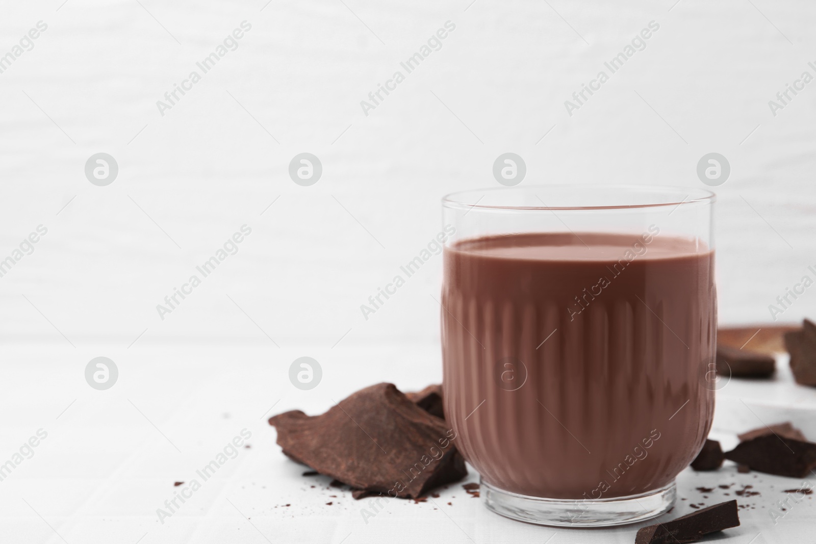 Tasty chocolate milk in glass and pieces of chocolate on white tiled table, closeup. Space for text Photo of Tasty chocolate milk in glass and pieces of chocolate on white tiled table, closeup. Space for text