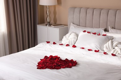 Photo of Heart made with beautiful rose petals on bed indoors