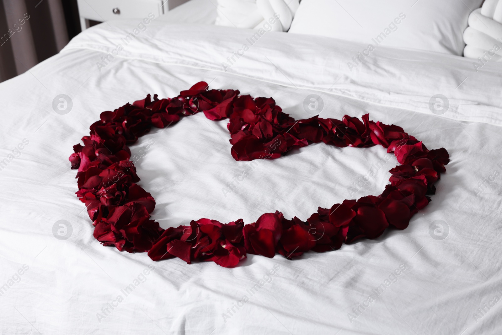 Photo of Heart made with beautiful rose petals on bed