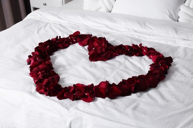 Photo of Heart made with beautiful rose petals on bed