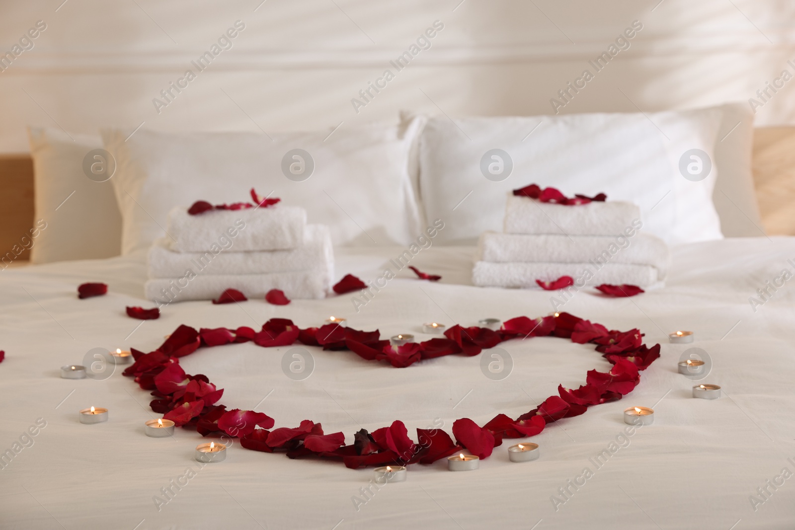 Heart made with rose petals and burning candles on bed indoors Photo of Heart made with rose petals and burning candles on bed indoors