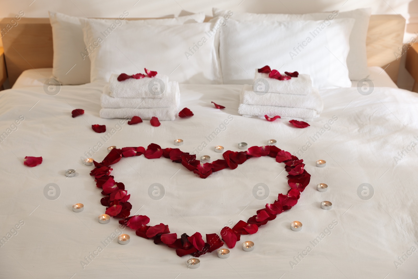 Heart made with rose petals and burning candles on bed indoors Photo of Heart made with rose petals and burning candles on bed indoors