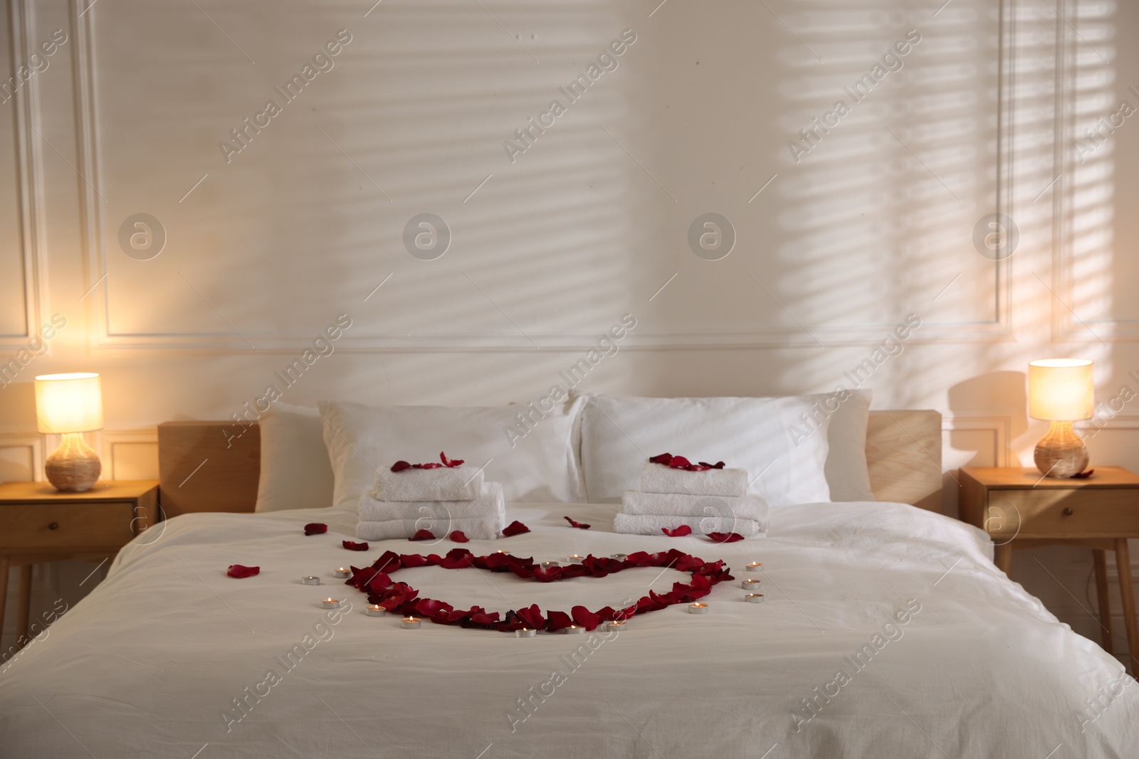 Heart made with rose petals and burning candles on bed indoors Photo of Heart made with rose petals and burning candles on bed indoors