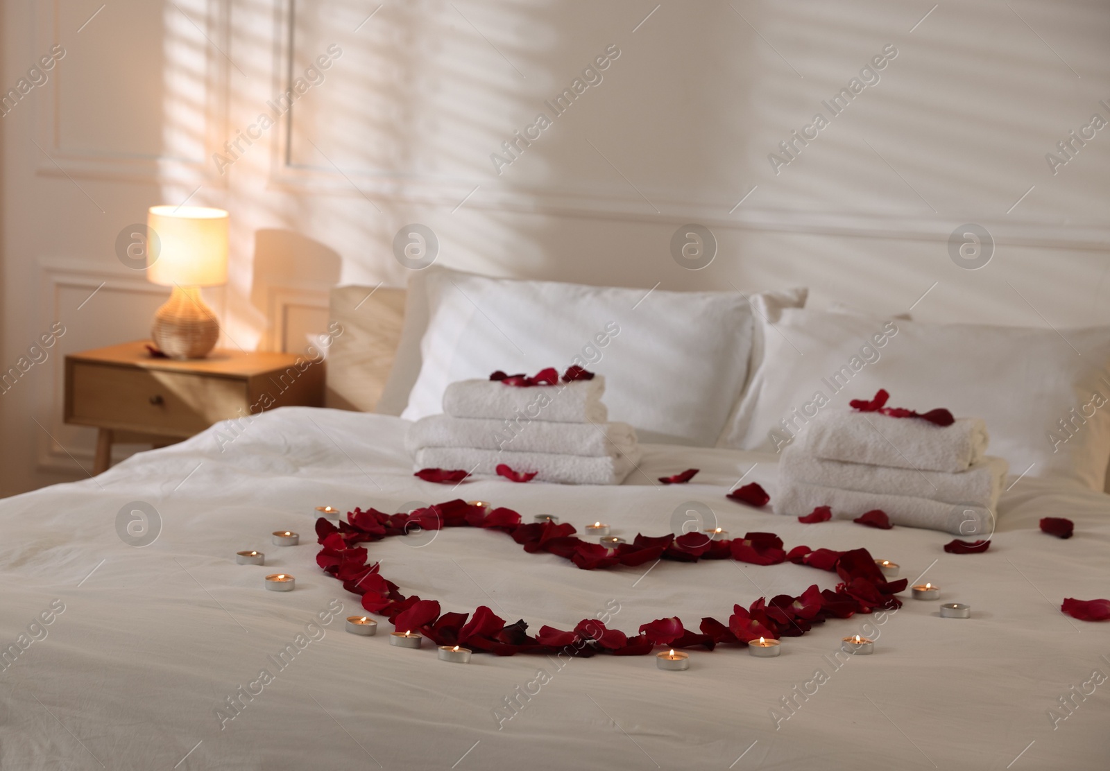 Heart made with rose petals and burning candles on bed indoors Photo of Heart made with rose petals and burning candles on bed indoors