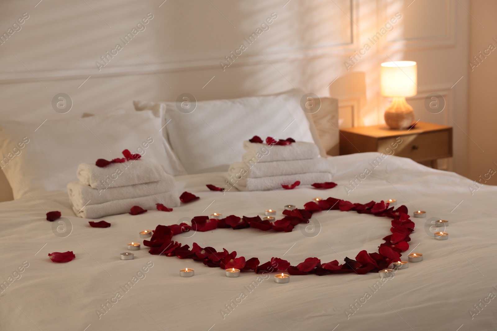 Heart made with rose petals and burning candles on bed indoors Photo of Heart made with rose petals and burning candles on bed indoors