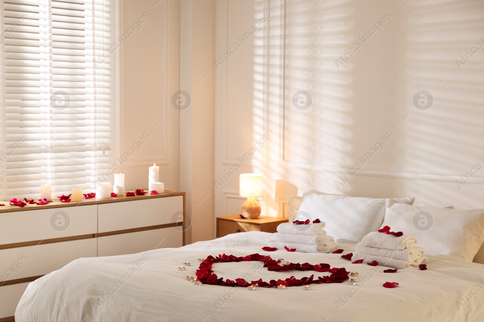 Heart made with rose petals and burning candles on bed indoors Photo of Heart made with rose petals and burning candles on bed indoors