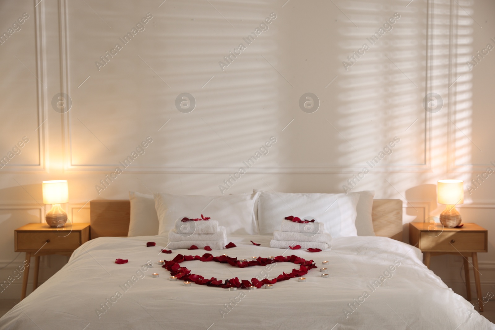 Heart made with rose petals and burning candles on bed indoors Photo of Heart made with rose petals and burning candles on bed indoors