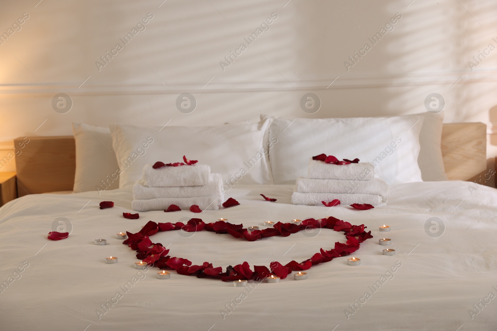 Heart made with rose petals and burning candles on bed indoors Photo of Heart made with rose petals and burning candles on bed indoors