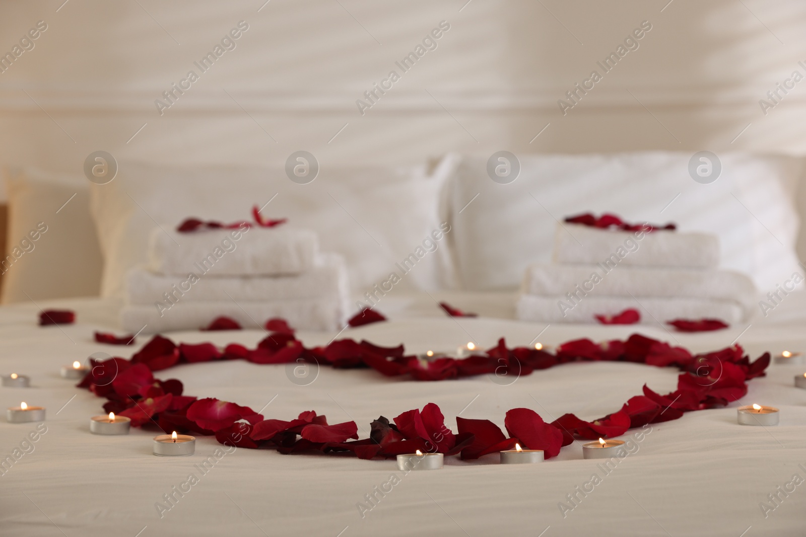 Heart made with rose petals and burning candles on bed indoors Photo of Heart made with rose petals and burning candles on bed indoors