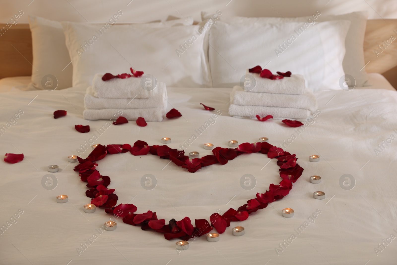 Heart made with rose petals and burning candles on bed indoors Photo of Heart made with rose petals and burning candles on bed indoors