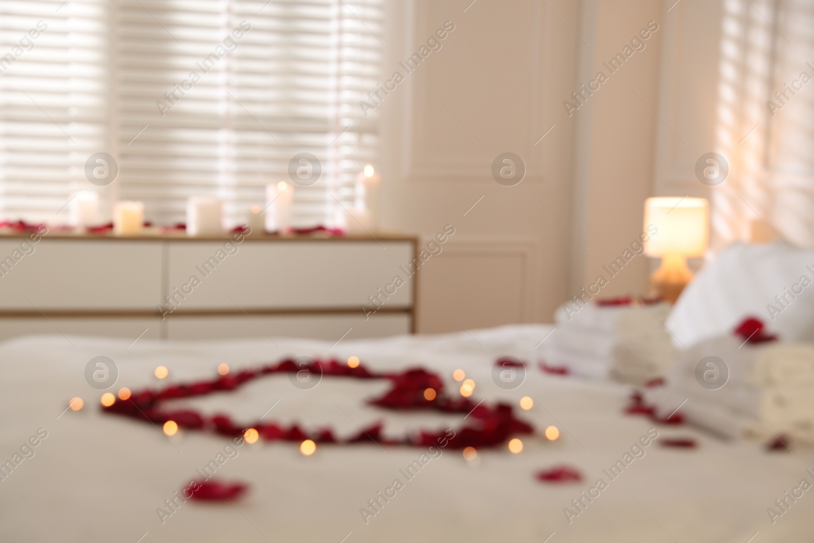 Heart made with rose petals and burning candles on bed indoors Photo of Heart made with rose petals and burning candles on bed indoors