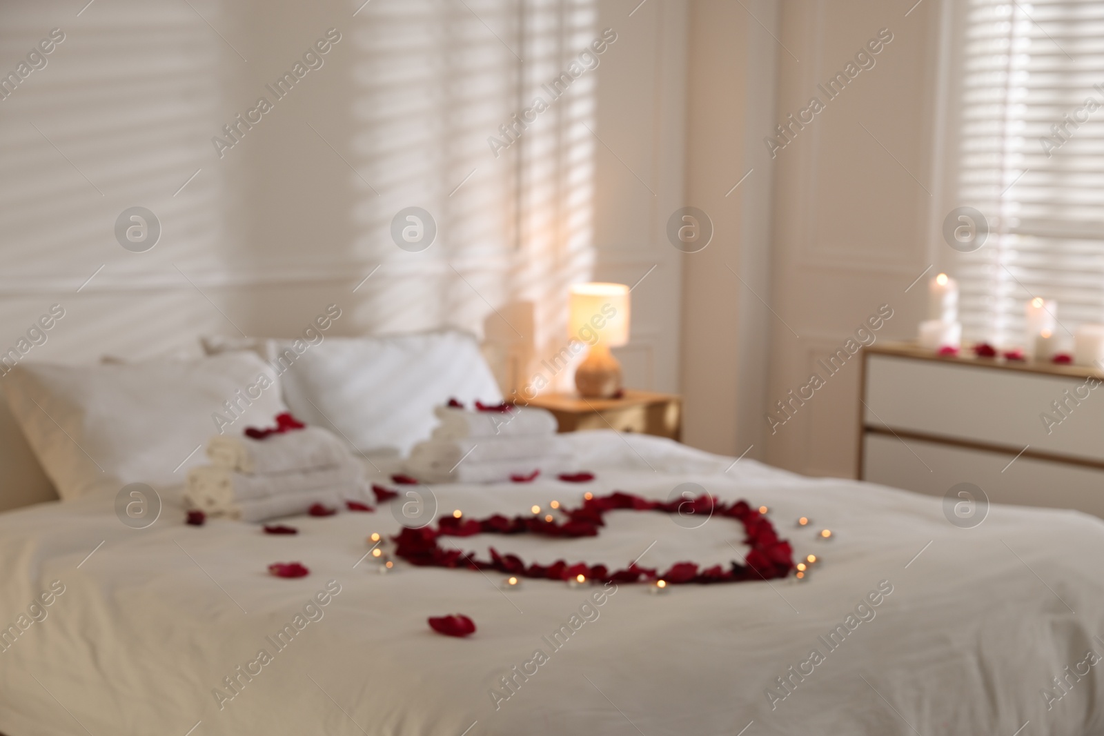 Heart made with rose petals and burning candles on bed indoors Photo of Heart made with rose petals and burning candles on bed indoors
