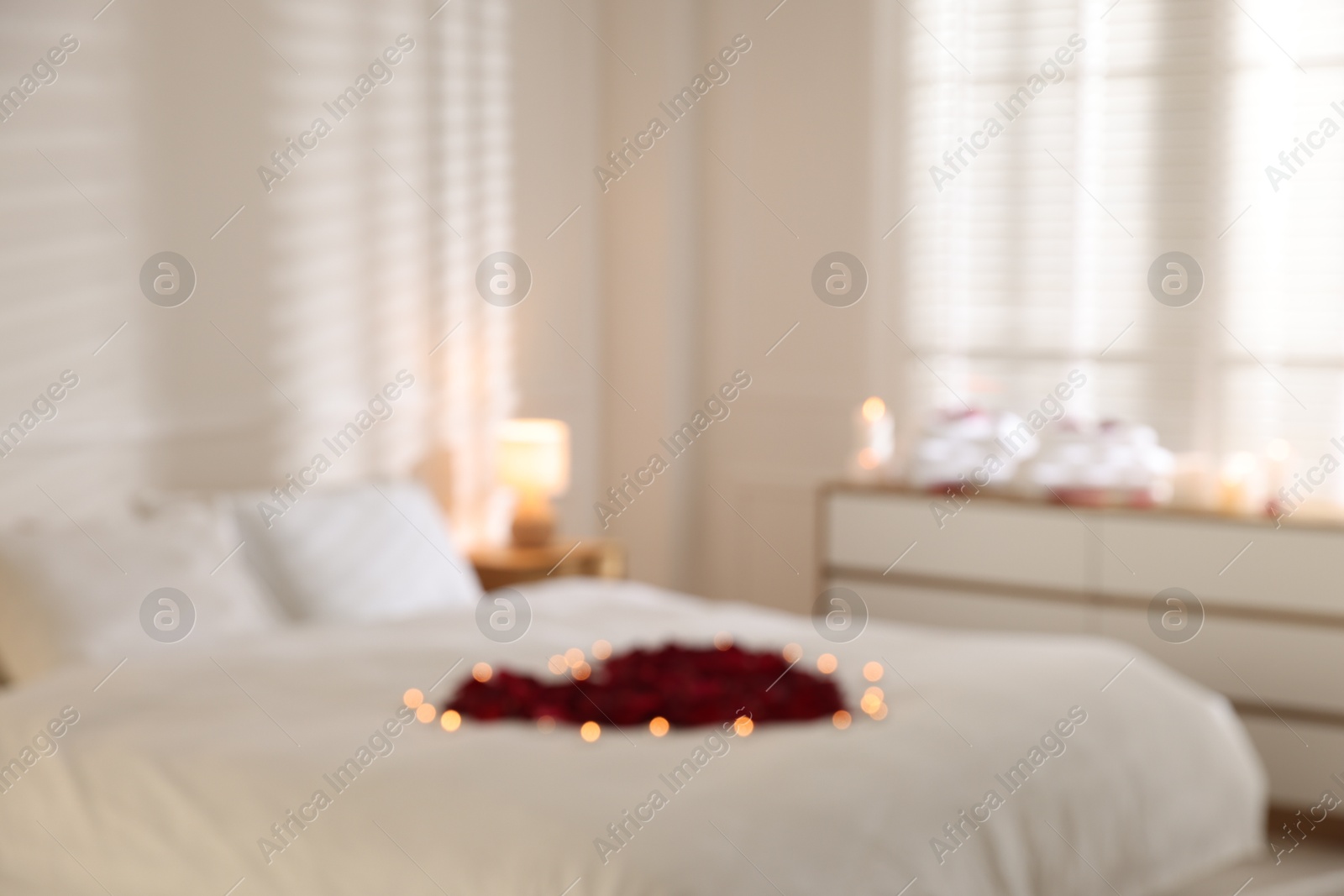 Blurred view of bed with flower heart and burning candles indoors Photo of Blurred view of bed with flower heart and burning candles indoors