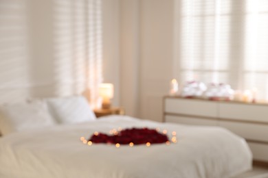 Photo of Blurred view of bed with flower heart and burning candles indoors