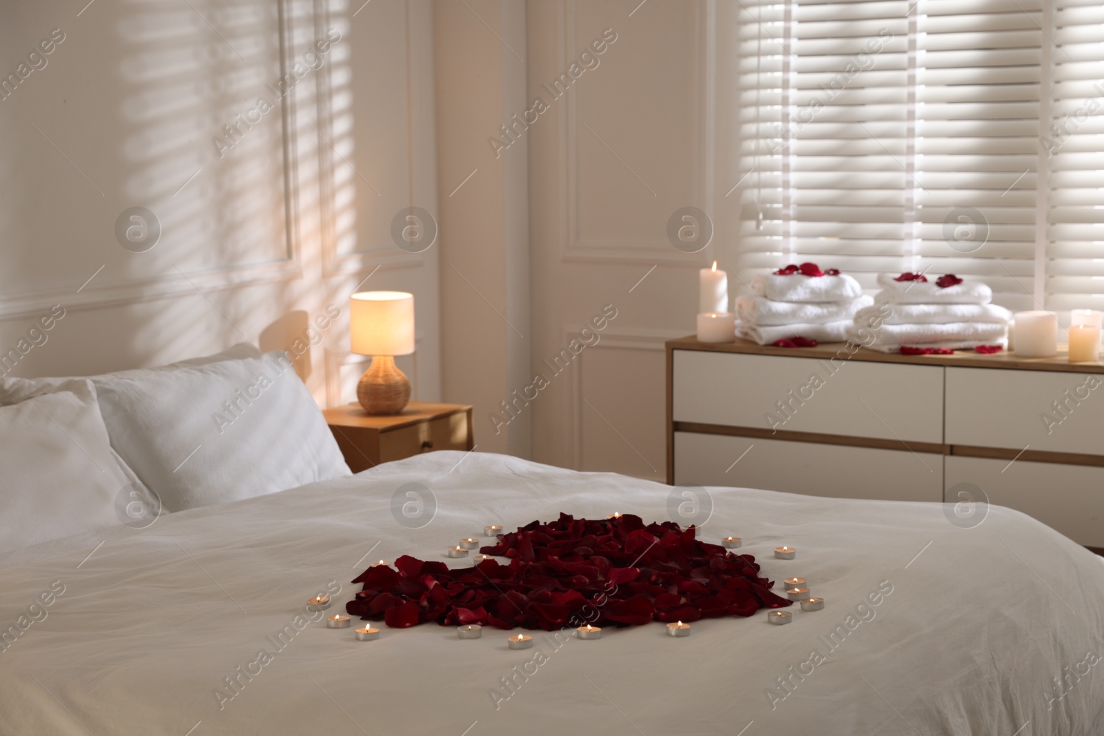 Heart made with rose petals and burning candles on bed indoors Photo of Heart made with rose petals and burning candles on bed indoors