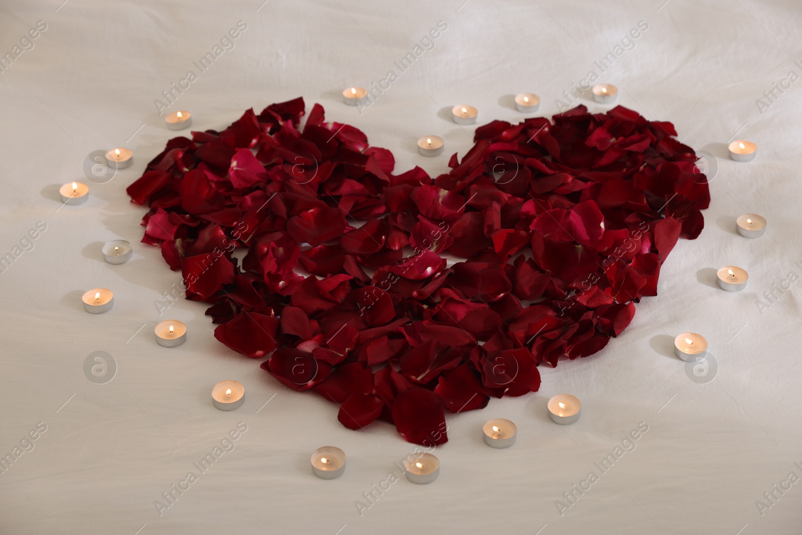 Heart made with rose petals and burning candles on bed, closeup Photo of Heart made with rose petals and burning candles on bed, closeup