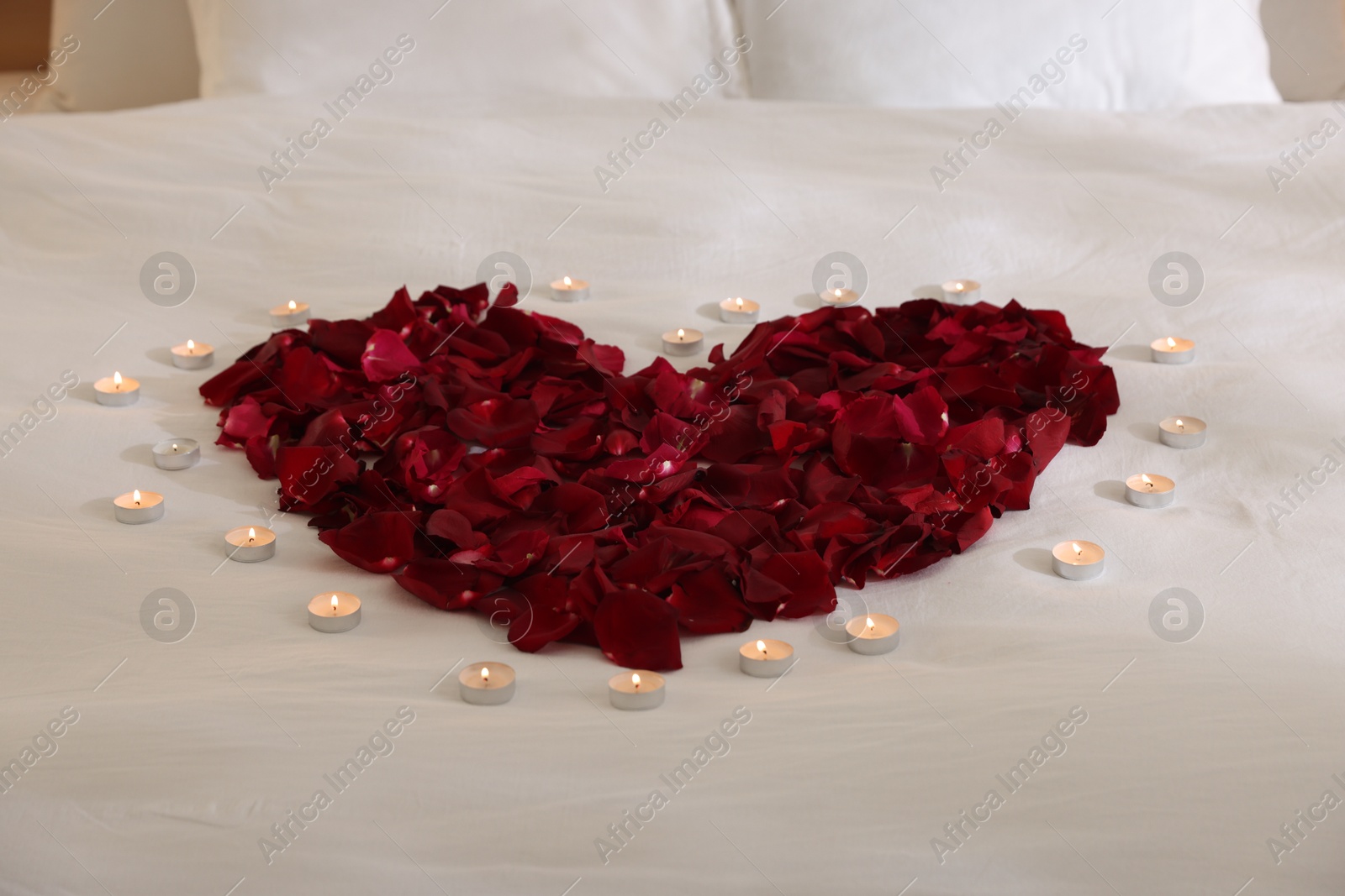 Heart made with rose petals and burning candles on bed, closeup Photo of Heart made with rose petals and burning candles on bed, closeup