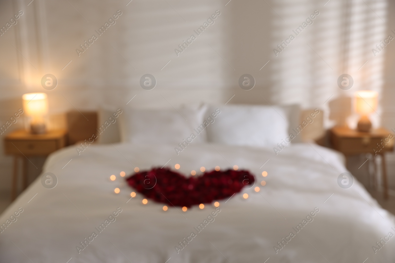 Heart made with rose petals and burning candles on bed indoors Photo of Heart made with rose petals and burning candles on bed indoors
