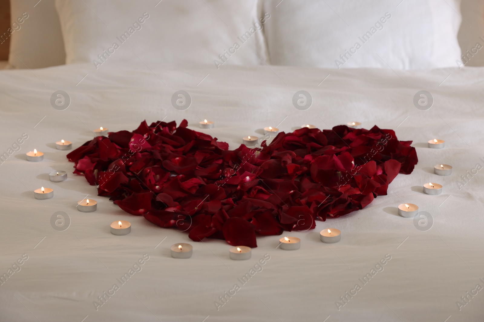 Heart made with rose petals and burning candles on bed, closeup Photo of Heart made with rose petals and burning candles on bed, closeup