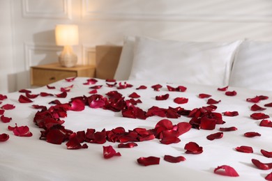 Photo of Heart made with rose petals on bed indoors, closeup