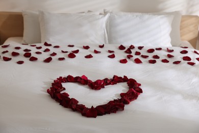 Photo of Heart made with rose petals on bed indoors, closeup
