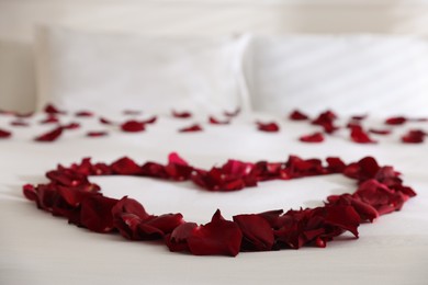 Photo of Heart made with rose petals on bed indoors, closeup